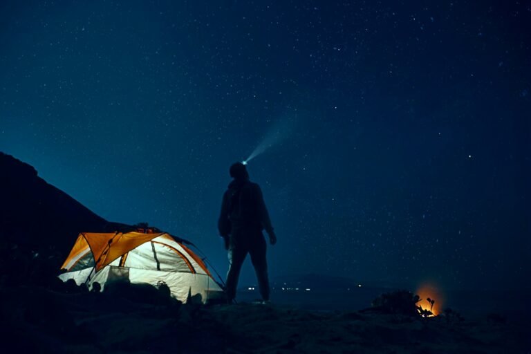 Illuminated tent and a camper wearing a headlamp beneath a starry night sky