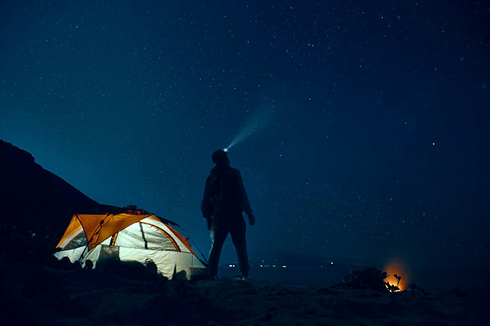 Illuminated tent and a camper wearing a headlamp beneath a starry night sky