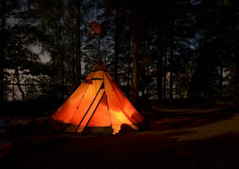 An orange illuminated tent among trees after dark, illustrating campsite lighting needs