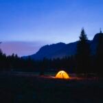 An illuminated tent in a mountain meadow at dusk, illustrating off-grid lighting needs