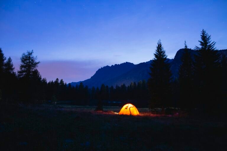An illuminated tent in a mountain meadow at dusk, illustrating off-grid lighting needs