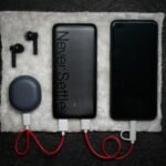 Black power bank connected by USB cables to a phone and an earbud charging case