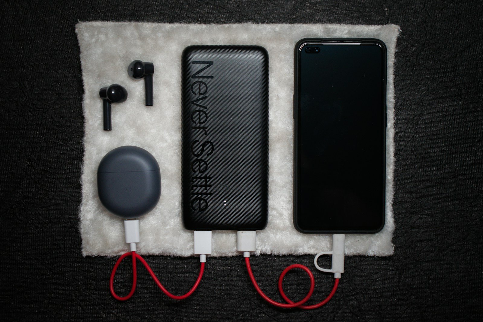 Black power bank connected by USB cables to a phone and an earbud charging case