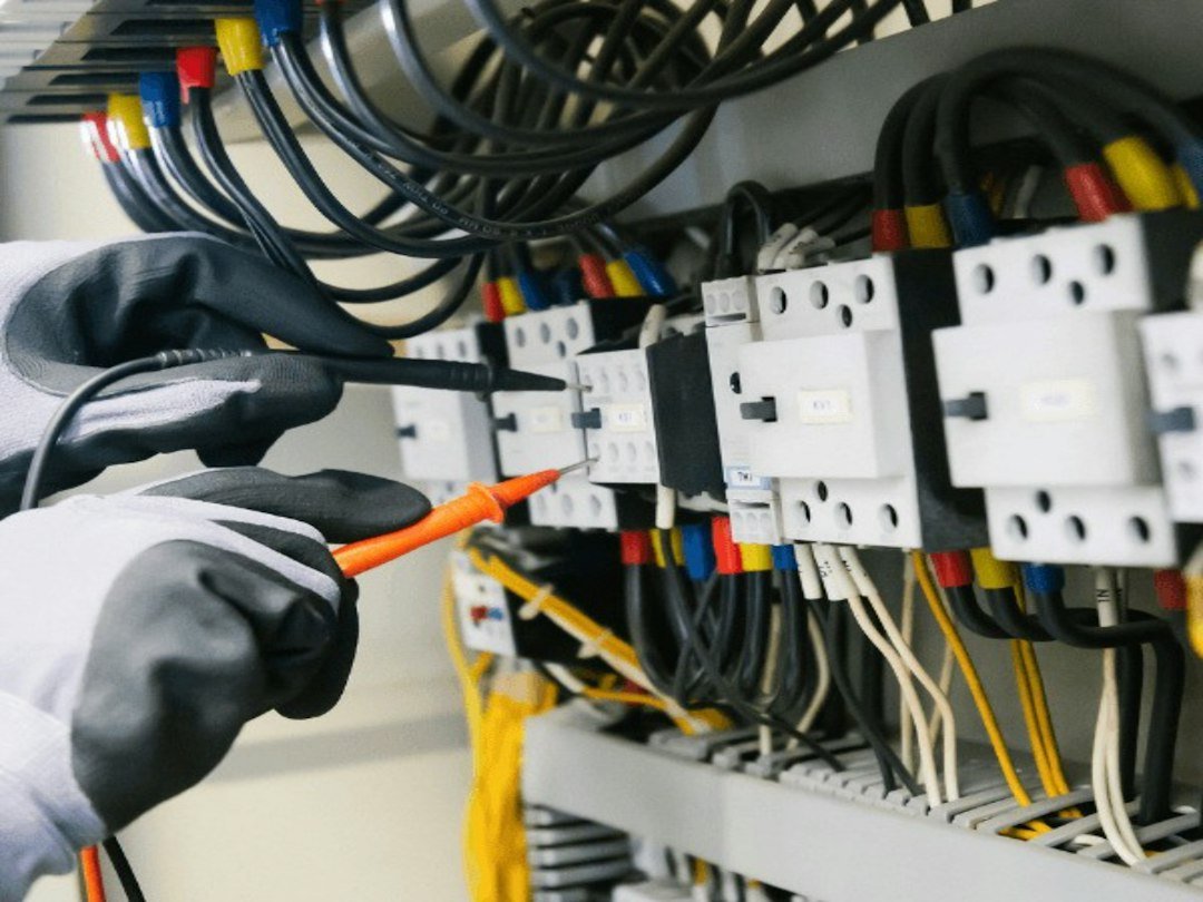 Electrician testing electrical equipment and wiring inside a control panel.