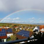 Houses with rooftop solar panels beneath a rainbow