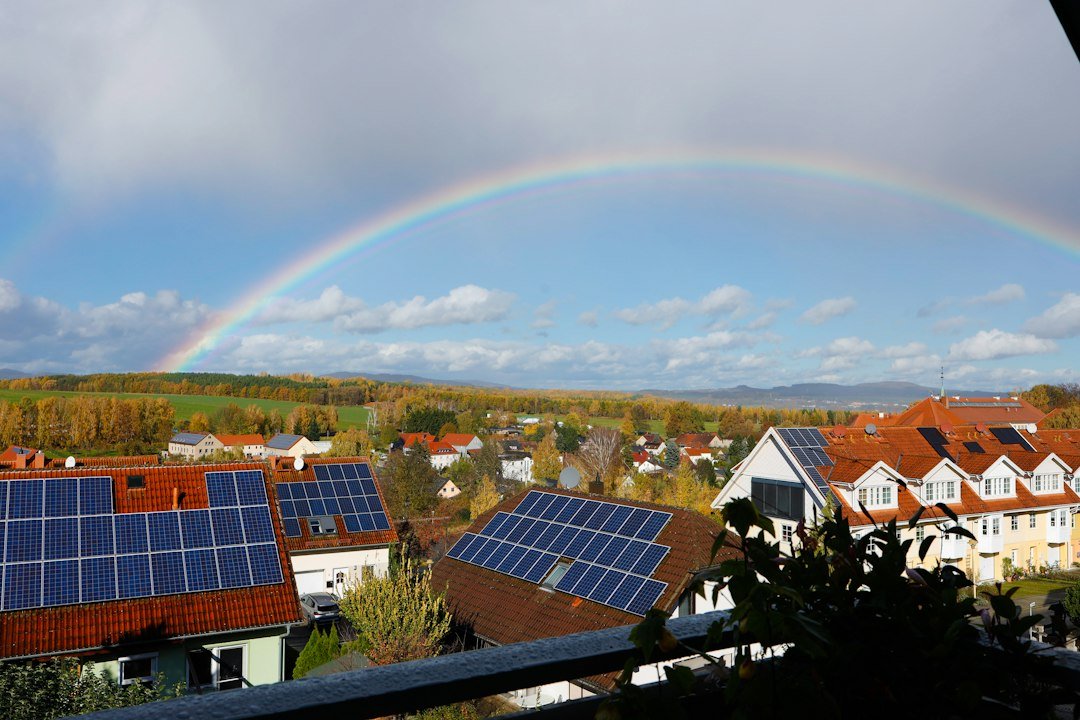 Houses with rooftop solar panels beneath a rainbow