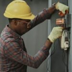 Electrician wearing a hard hat works on an electrical panel